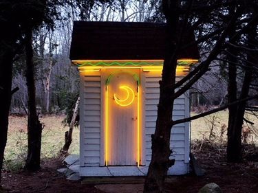 An outhouse with a neon moon symbol on the door
