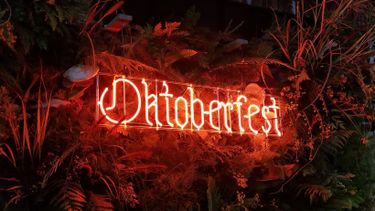 Neon sign surrounded by foliage reads Oktoberfest